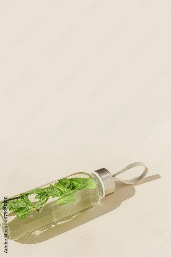 Fototapeta premium Glass bottle with green mint leaves water drink detox at sunlight on beige table background, copy space, sun glare. Natural Infused water Healthy drink. Aesthetic still life, refreshing drink