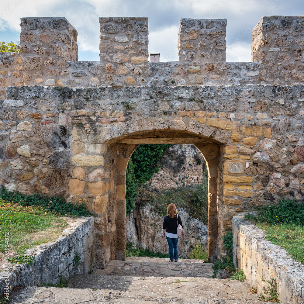 Tourist woman exiting through an arched gate of the wall of the medieval city of Frias, Burgos.