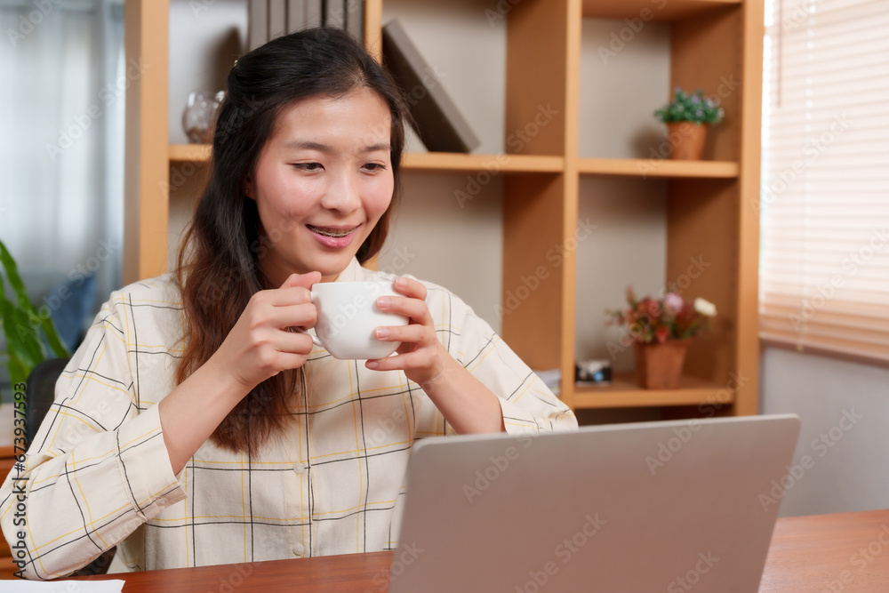 Asian woman working on laptop, placed on desk in office room, because was sleepy, brought coffee drink while working relieve sleepiness, when drank coffee became more alert. Asian woman working on laptop, placed on desk in office room, because was sleepy, brought coffee drink while working relieve sleepiness, when drank coffee became more alert.