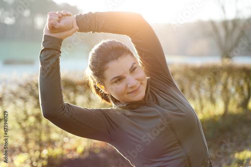 Beautiful sporty athletic young woman doing stretching exercises on a cold sunny morning in winter or autumn
