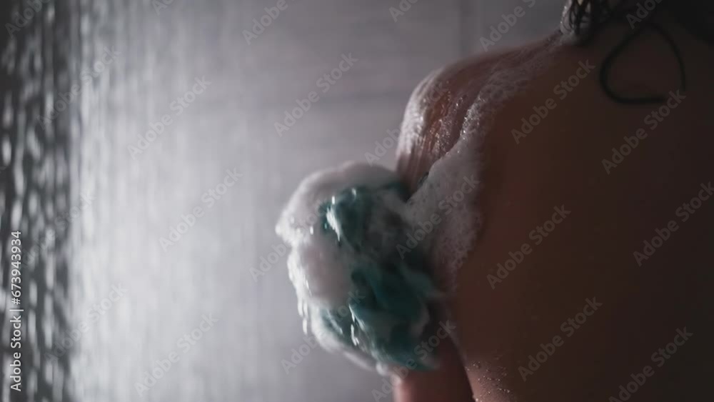 Woman rubs skin with loofah in shower cabin closeup. Lady washes body with soft foamy sponge near falling water drops. Skincare and massage tool Woman rubs skin with loofah in shower cabin closeup. Lady washes body with soft foamy sponge near falling water drops. Skincare and massage tool