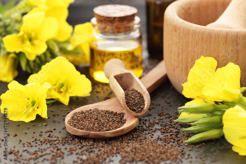 Foto Evening primrose seeds and oil in glass bottle with flowers  on black background