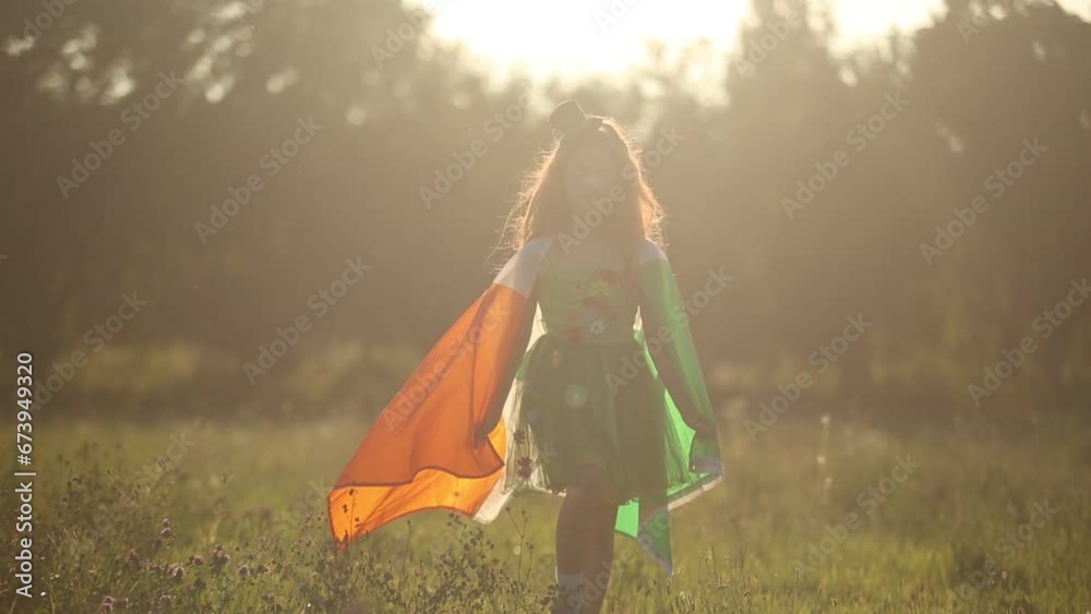 Cute redhead girl dressed as a green fairy walking outdoors with flag of Ireland on shoulders. Irish child celebrating St Patricks Day