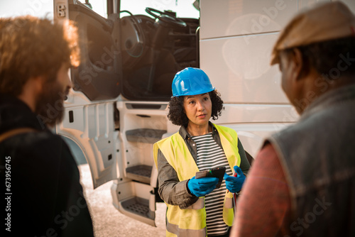 Woman logistic worker talking to truck drivers on parking lot photo