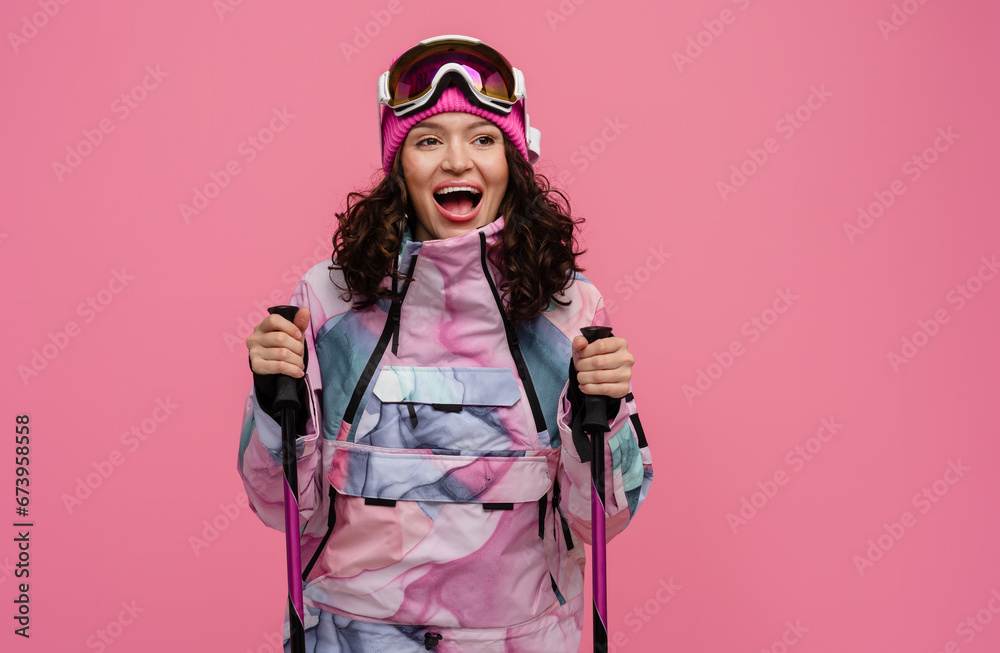 attractive smiling woman posing on pink background with skis in snow winter skiing sport suit