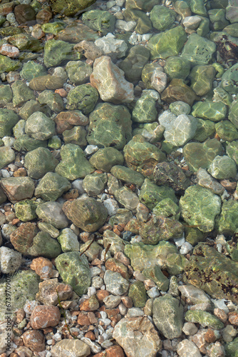 Transparent clear sea water and green stones on the beach abstract water background