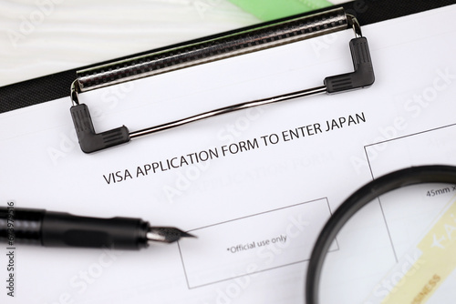Visa application to enter Japan on A4 tablet lies on office table with pen and magnifying glass close up