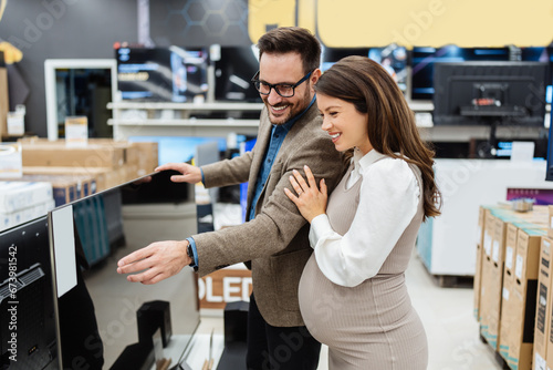 Beautiful and happy middle age couple buying consumer tech products in modern home appliances store. They are choosing home theater and TV devices. People and consumerism concept.