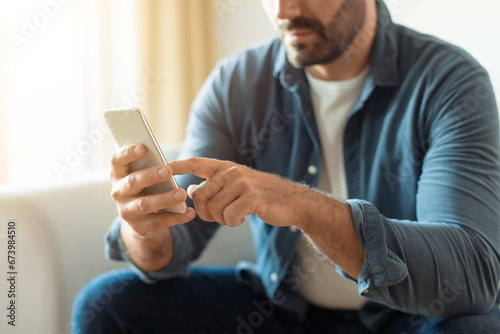 Unrecognizable middle aged man in casual using smartphone sitting indoor
