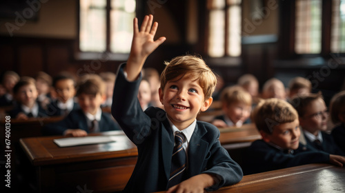 student at a desk in a school class raises his hand, child, smart kid, children, study, learning, classroom, knowledge, lesson, pupil, schoolboy, boy, uniform, european, tie, smile, portrait, face photo