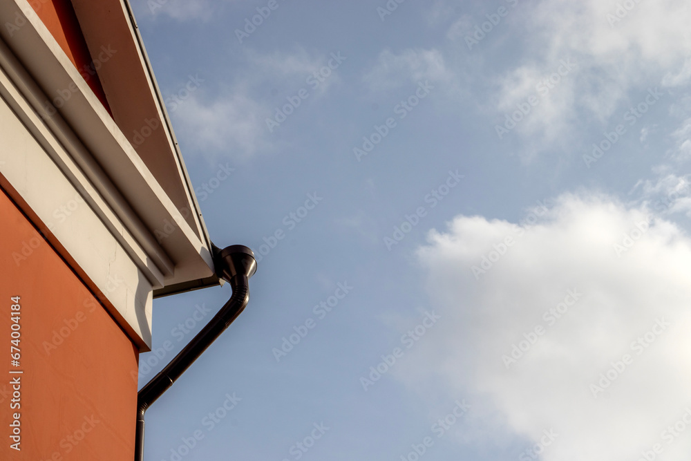 Bottom view of the corner of the building against the blue sky. Abstract view of the corner of the wall and sky. Drain pipes of the roof of a building against the background of a bright sky. Bottom view of the corner of the building against the blue sky. Abstract view of the corner of the wall and sky. Drain pipes of the roof of a building against the background of a bright sky.