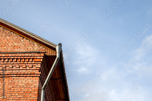 Bottom view of the corner of the building against the blue sky. Abstract view of the corner of the wall and sky. Drain pipes of the roof of a building against the background of a bright sky.
