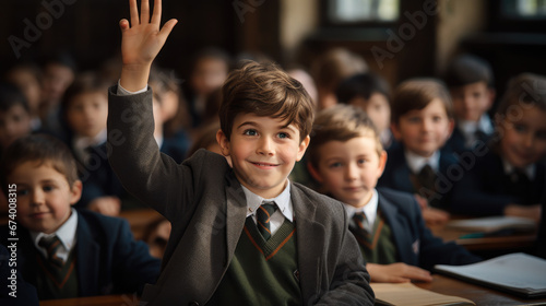 student at a desk in a school class raises his hand, child, smart kid, children, study, learning, classroom, knowledge, lesson, pupil, schoolboy, boy, uniform, european, tie, smile, portrait, face