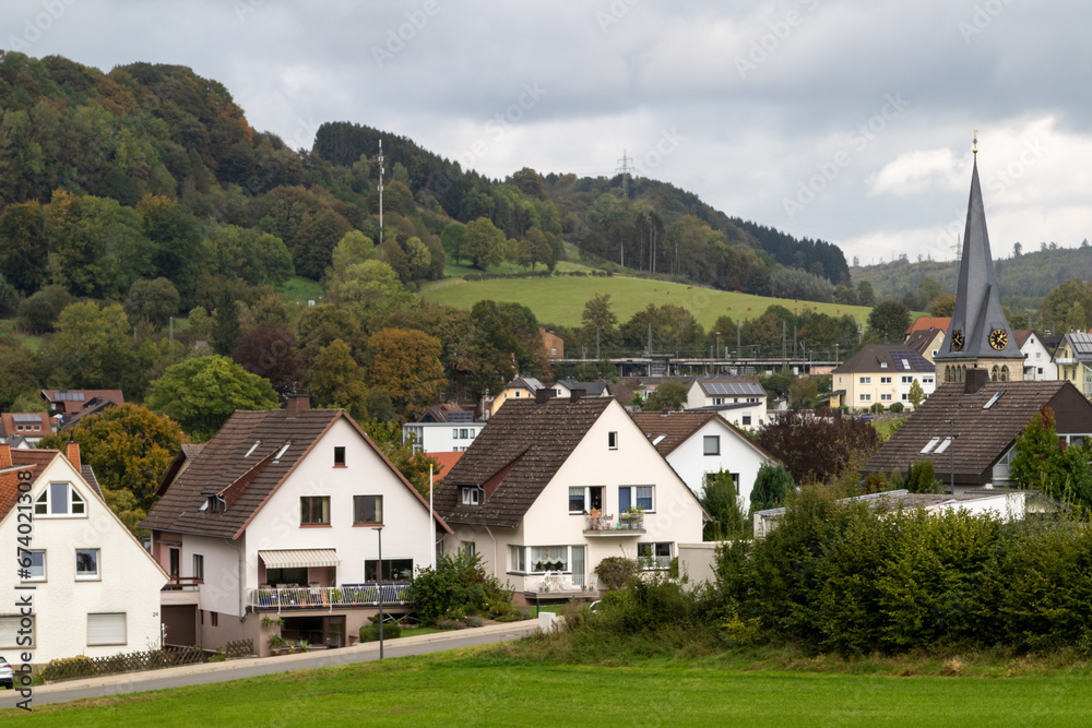 village in the mountains, images shows a small village in germany near the town of paderborn, consisting of few houses, shops and a church with spire, with the steep hills and trees in the background