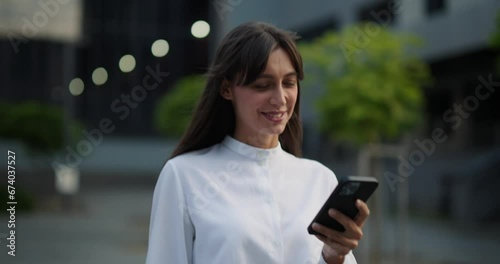 Woman in white shirt having a walk outdoor, using modern smartphone.