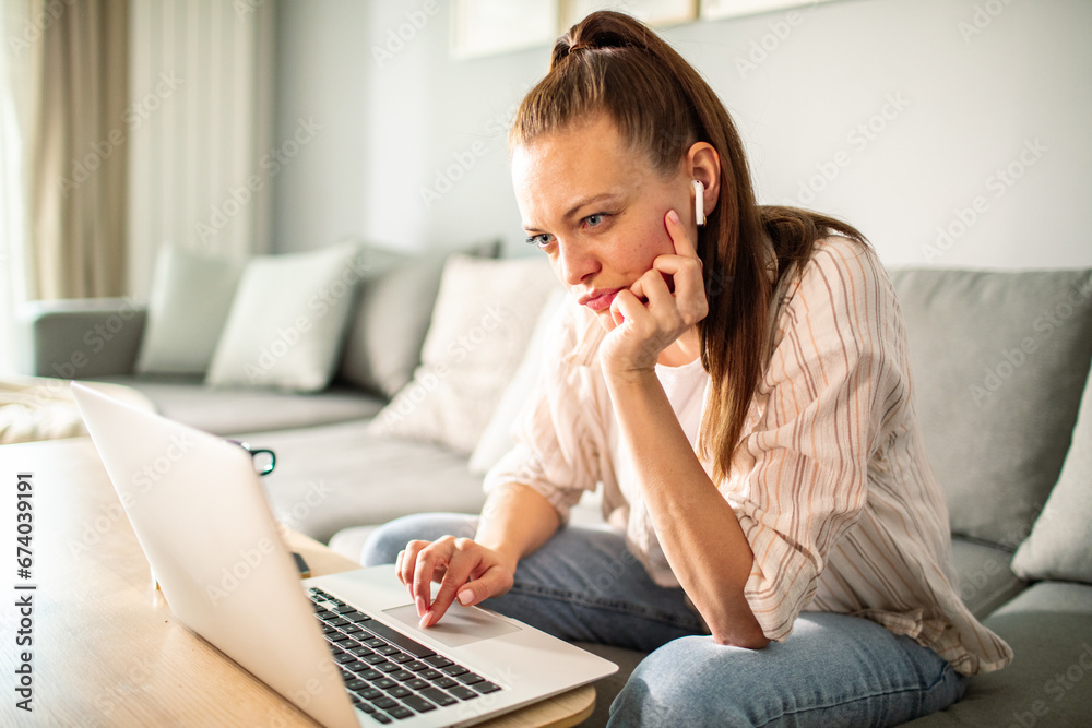 Thoughtful young woman using laptop at home
