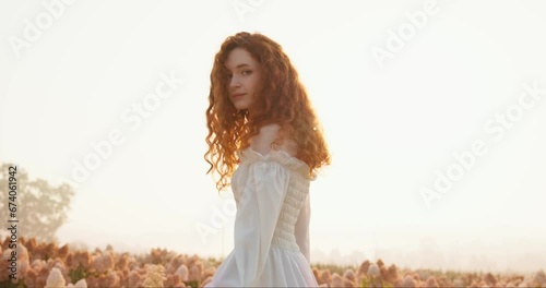 Beautiful red-haired woman in white sophisticated dress having a walk-in field