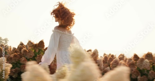 Beautiful red-haired woman in white sophisticated dress running on field