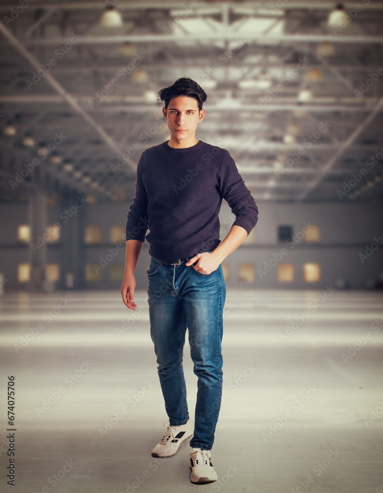 Young man walking in large modern empty storehouse, looking at camera, full body shot Young man walking in large modern empty storehouse, looking at camera, full body shot