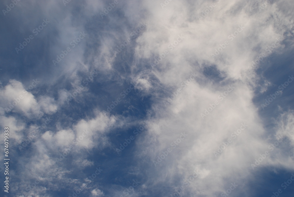 Aerial landscape on a summer day. High cirrus and low cumulus clouds hang in the light blue sky. They are at different levels and in different sizes. The blue sky is visible among the clouds.