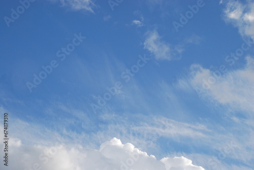 Aerial landscape on a summer day. High cirrus and low cumulus clouds hang in the light blue sky. They are at different levels and in different sizes. The blue sky is visible among the clouds.