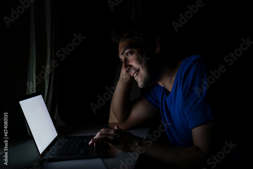 Side view of young handsome man working on laptop at night. Work from home concept	