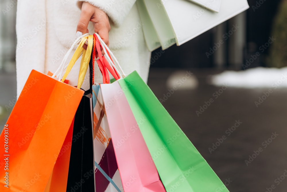 Cropped image european woman hold hand colorful bags woman walking after shopping dressed warm coat scarf retail store near mall on the street sales black friday season 