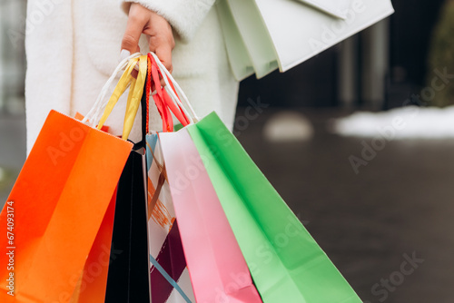 Cropped image european woman hold hand colorful bags woman walking after shopping dressed warm coat scarf retail store near mall on the street sales black friday season 