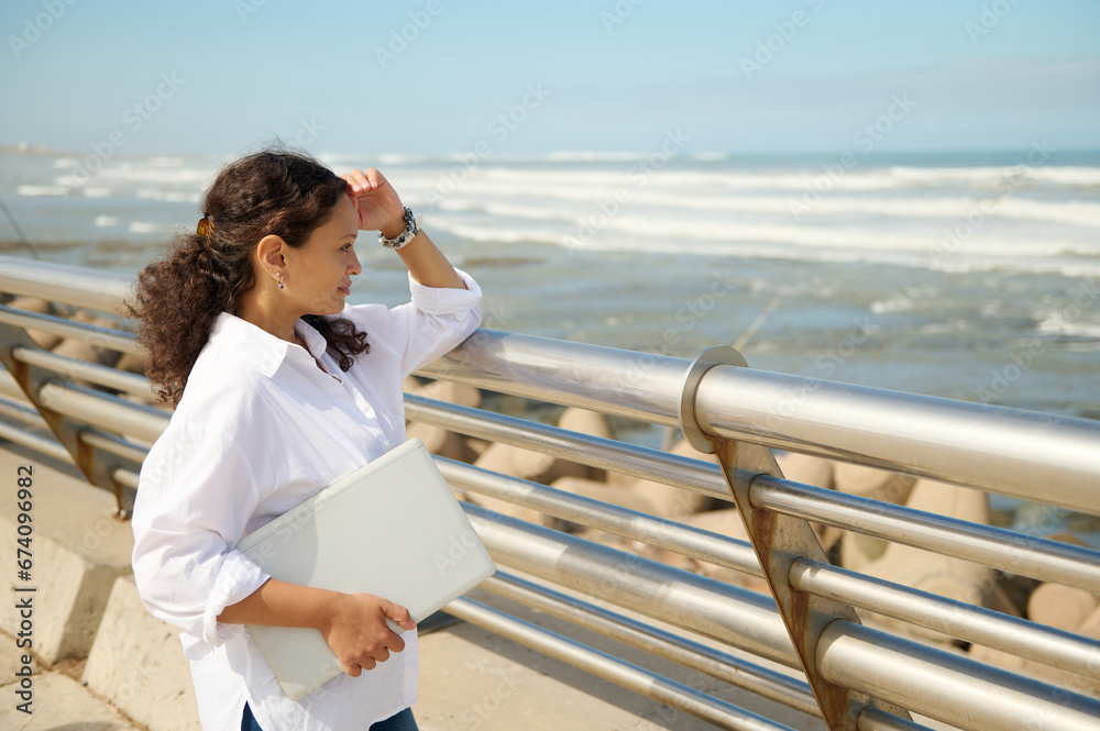 Young adult business woman freelance entrepreneur holding laptop and admiring the seashore while a coffee break outdoors Young adult business woman freelance entrepreneur holding laptop and admiring the seashore while a coffee break outdoors