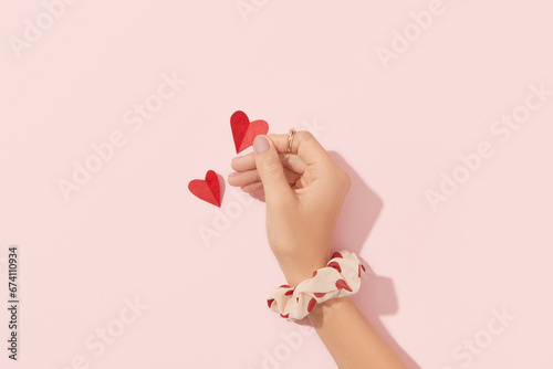 Beautiful well-groomed female hand with pink matte nails holding paper heart on a pink background. Valentines Day concept