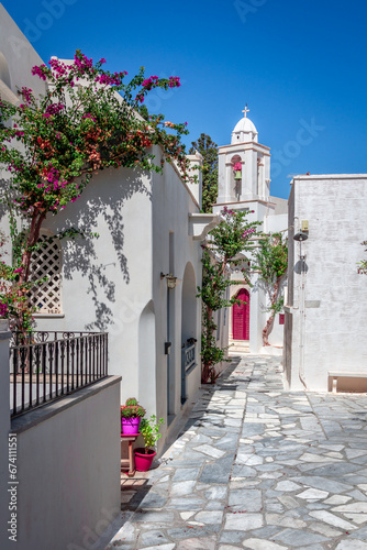 Narrow cobblestone alley, whitewashed houses, whitewashed orthodox church and bougainvilleas. Summertime in Pyrgos, a mountainous village in Tinos Island, Cyclades, Greece. photo