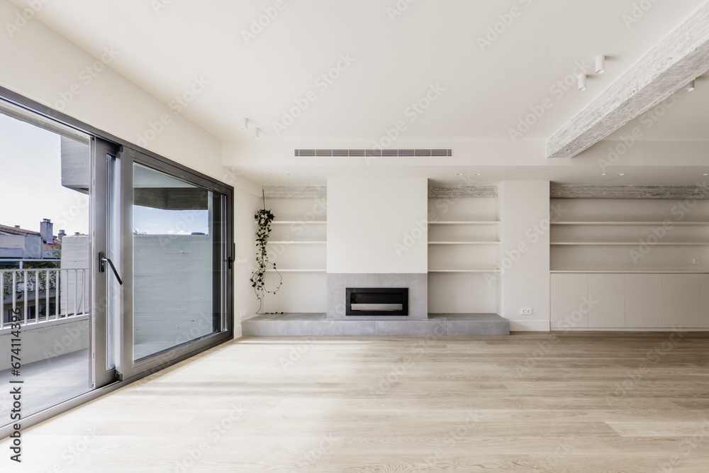 Fototapeta premium Front image of the living room of a recently renovated modern home with built-in furniture on one side, gray fireplace, wooden floors and terrace with views of the neighbors