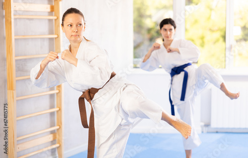Young woman and adult woman in kimono training karate techniques in studio