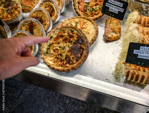 Paris, France. June 30 2022. At the beautiful Marché Popincourt local market, a food stall with French savory pie specialities. A customer's hand indicates which one to buy. photo