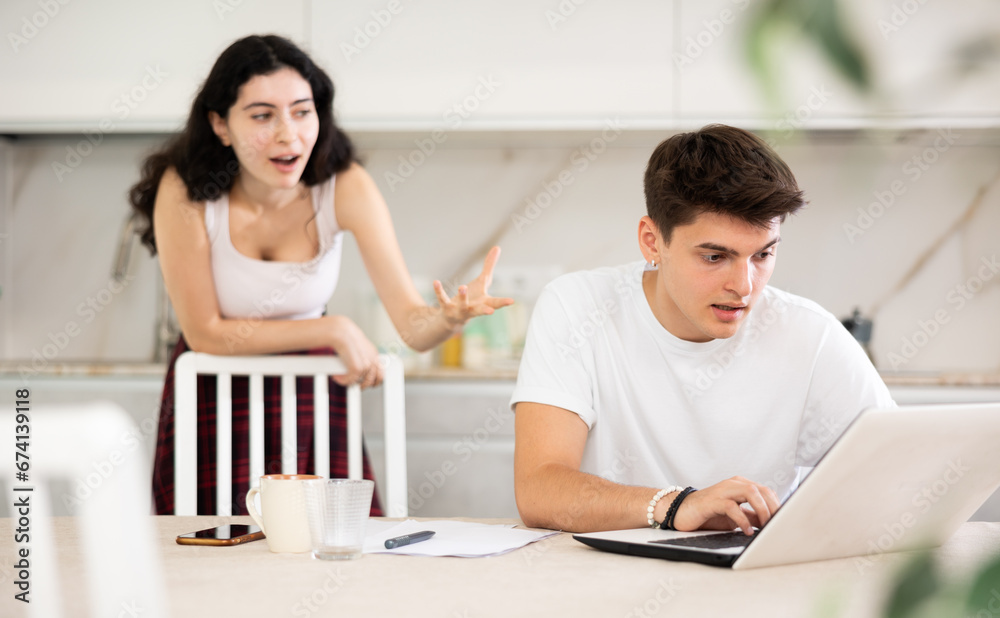 Obraz premium Young woman screams during family quarrel with young guy using laptop in kitchen