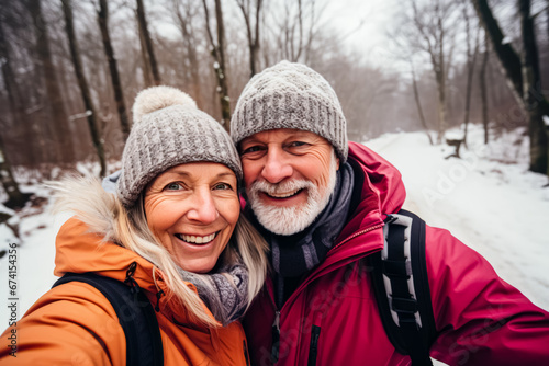 portrait of happy senior couple taking selfie photo while enjoying hike in winter forest