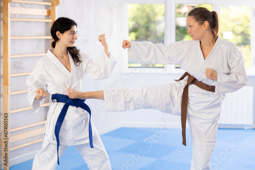 Adult woman and young woman in kimono doing karate exercises in gym