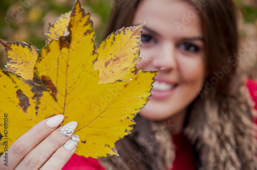 Portrait of a young attractive long haired brunette in the park covering her face with maple leaf