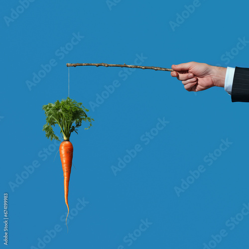 Businessman hand dangling a carrot on a stick against a blue sky background