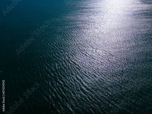 An aerial view of a majestic expanse of blue sea with lapping waves, the bright glint of the sun reflecting off the water