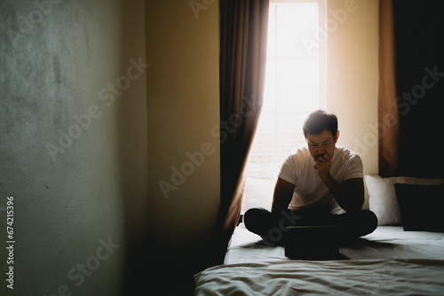 Lonely single man sit and rest alone in dark bedroom with light from curtain.