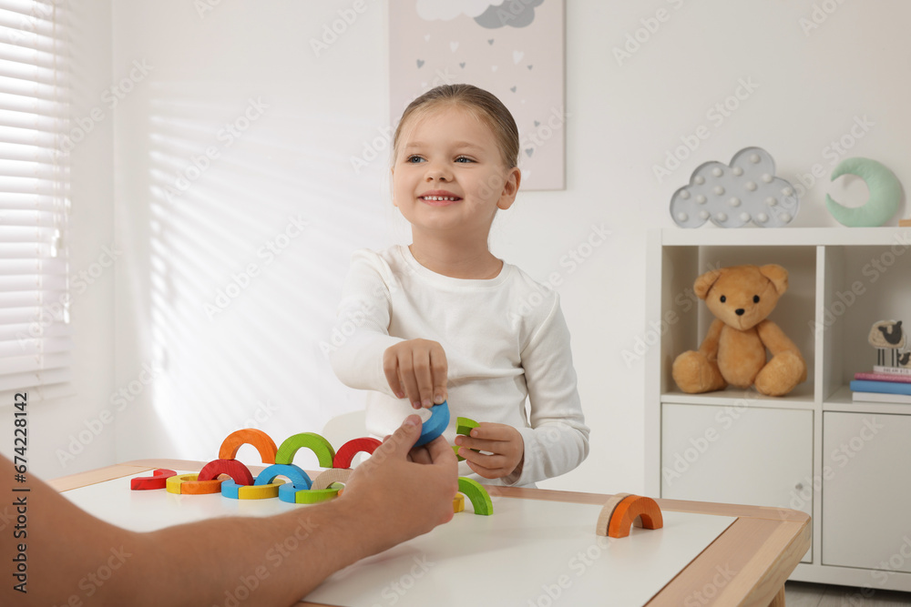 Motor skills development. Father helping his daughter to play with colorful wooden arcs at white table in room Motor skills development. Father helping his daughter to play with colorful wooden arcs at white table in room