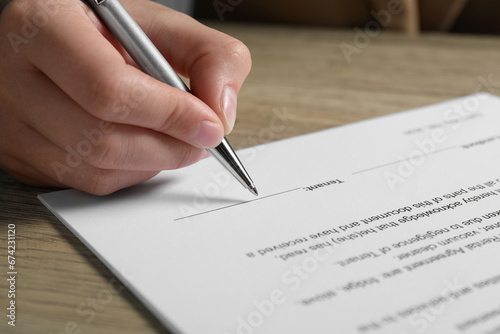 Woman signing document with pen at wooden table, closeup
