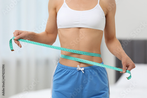 Slim woman measuring waist with tape at home, closeup. Weight loss