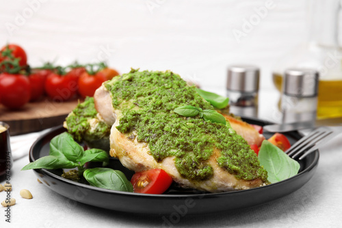 Delicious chicken breasts with pesto sauce, tomatoes and cutlery served on light table, closeup