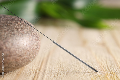 Acupuncture needle and spa stone on wooden table, closeup