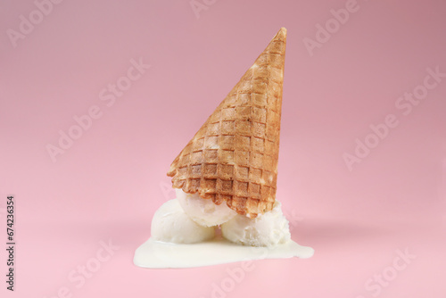 Melting ice cream and wafer cone on pink background