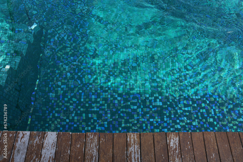 Clear rippled water in swimming pool and wooden deck outdoors, above view. Space for text