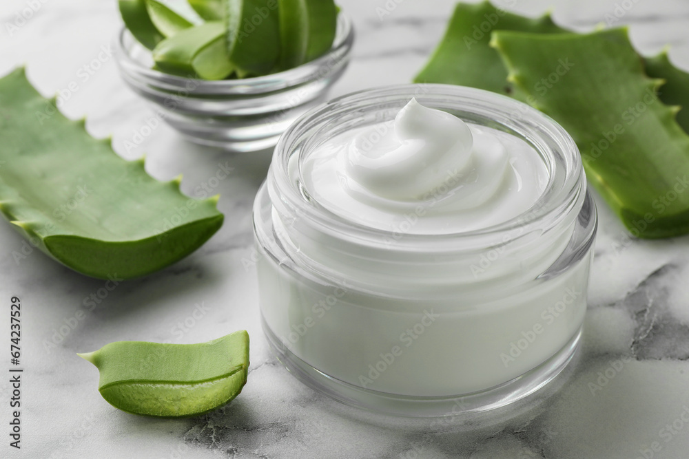 Jar with cream and cut aloe leaves on white marble table, closeup Jar with cream and cut aloe leaves on white marble table, closeup