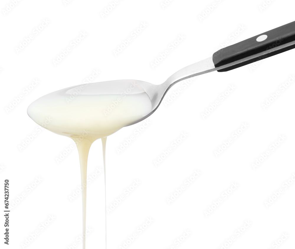 Pouring condensed milk from metal spoon isolated on white Pouring condensed milk from metal spoon isolated on white